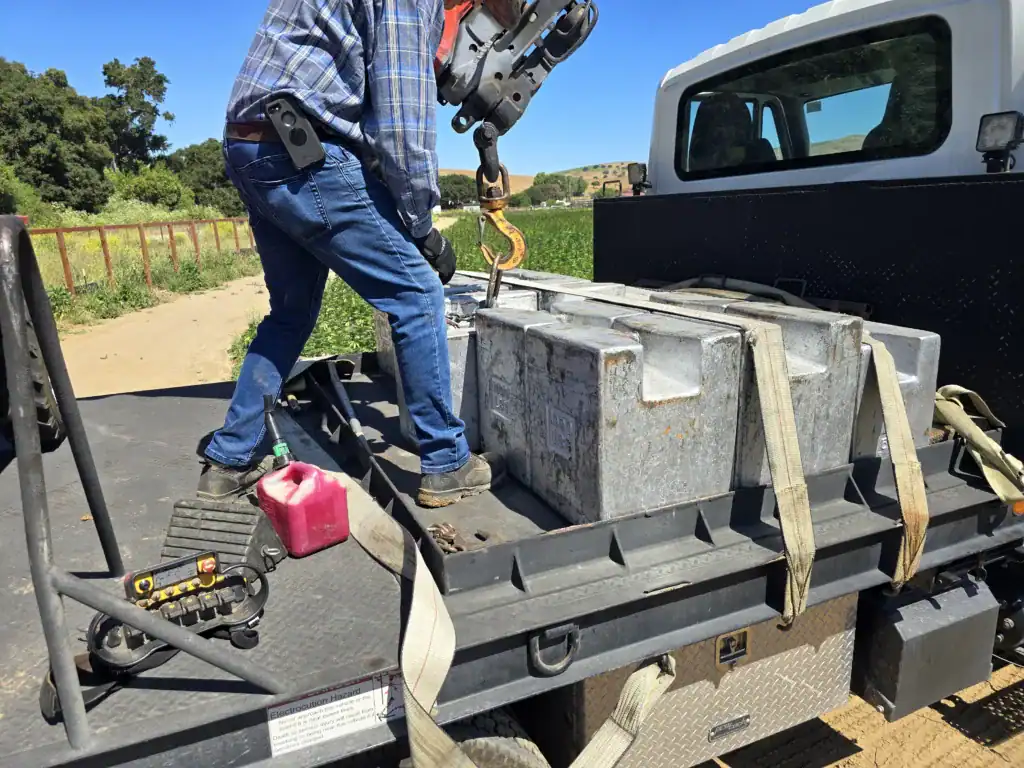 Cast-iron 1,000 lb reference weights strapped on a boom-truck bed while a technician hooks one to the crane